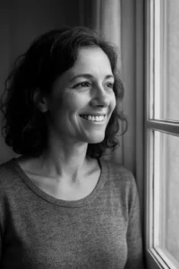 Photographie en noir et blanc d'une femme souriante regardant par la fenêtre. Elle symbolise la victoire et la renaissance après une séparation amoureuse grâce au coaching.